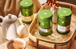 Trois boîtes vertes de thé Palais des Thés sur un plateau en osier, théière et tasse à côté.