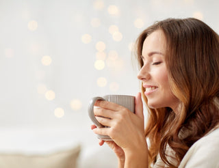 Femme souriante appréciant une tasse de thé chaud, ambiance cosy, lumière douce en arrière-plan.