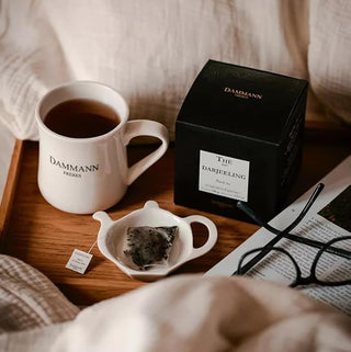 Tasse de thé Darjeeling avec boîte, sachet infusé et magazine sur un plateau en bois.