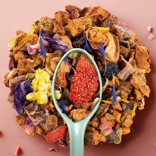 Mélange de thé en vrac avec fruits secs, fleurs colorées et une cuillère verte sur fond rose